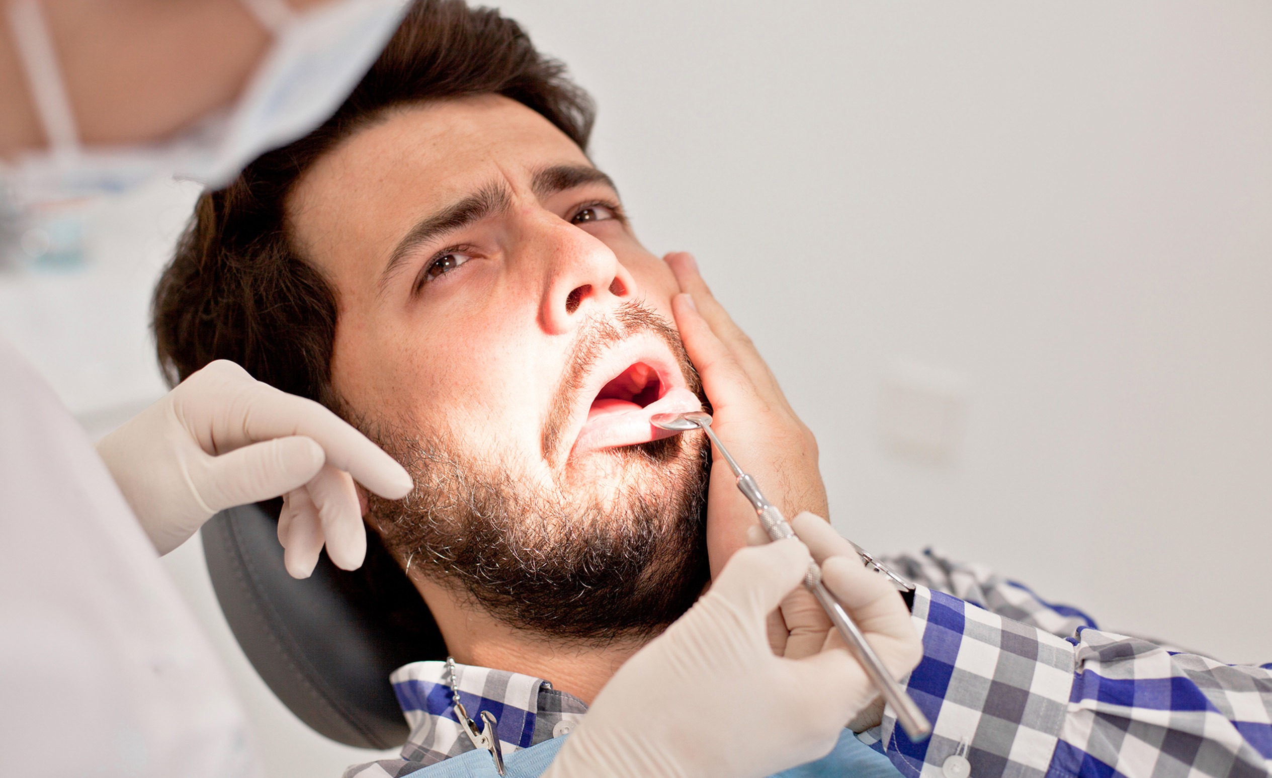 Fogorvos vizsgál egy férfit, aki fogja a fejét érzékeny foga miatt.
