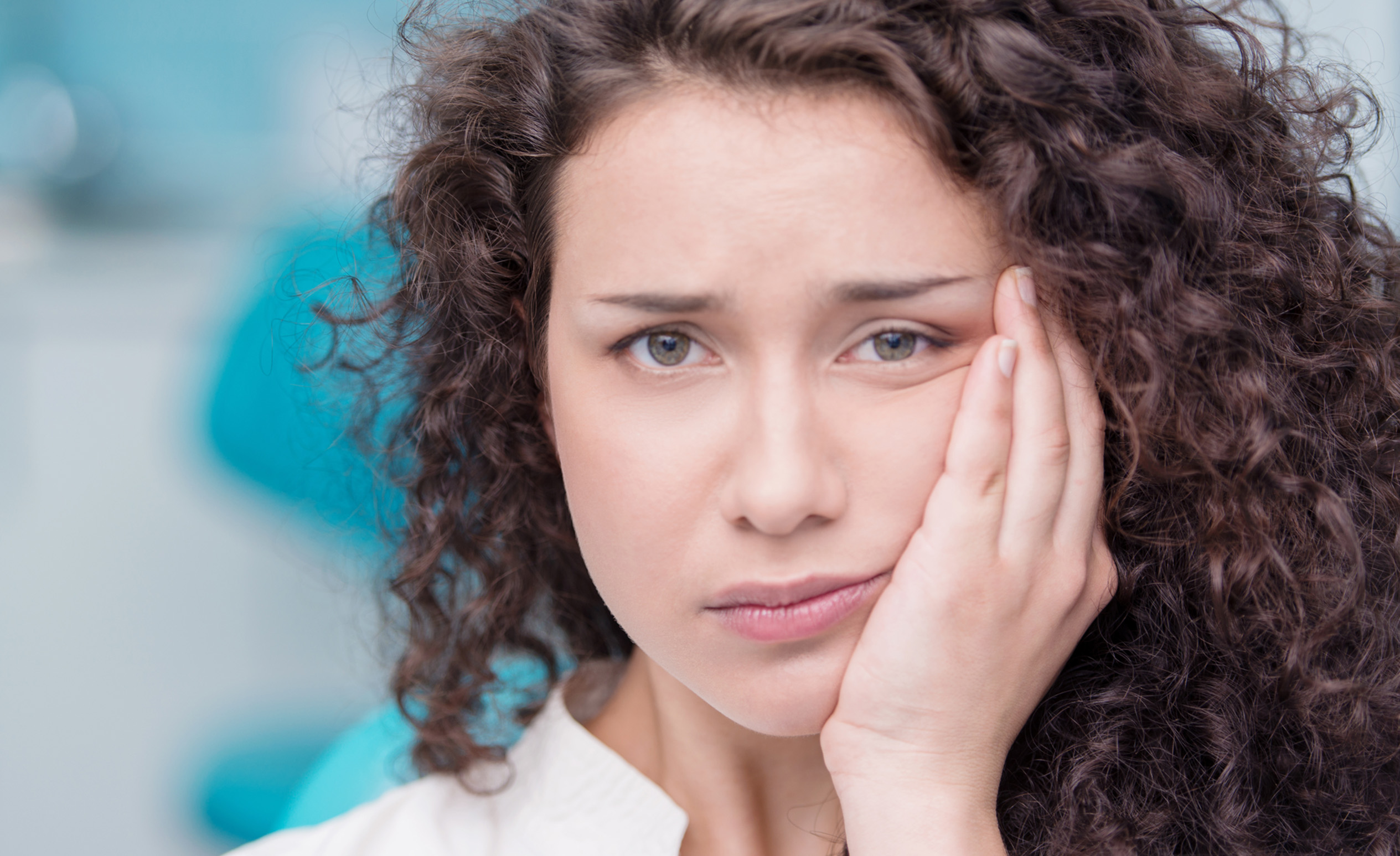 Barna hajú nő fogja az arcát mert nagyon fáj neki a foga.