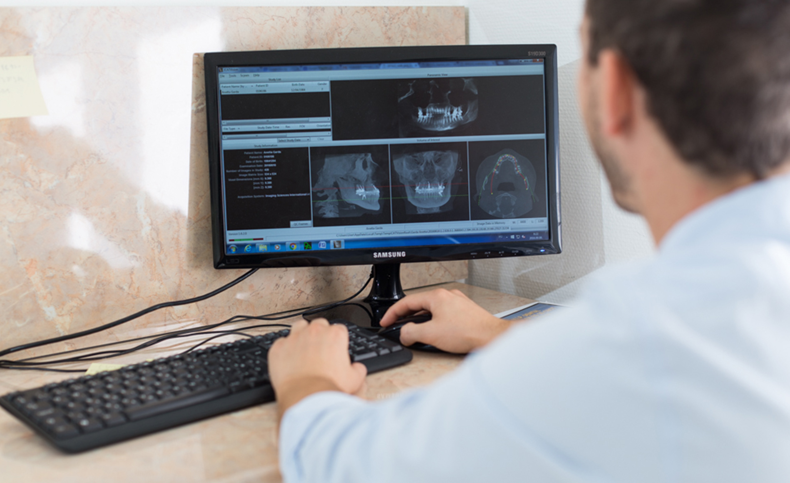 Dr. Varajti Artúr budapesti fogorvos, szájsebész ül a számítógép előtt és fogbeültetést támogató programot használ.