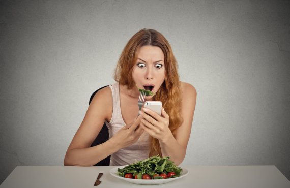 Vörös hajú nő eszik egy salátát, telefonon rossz híreket ad és döbbent arcot vág.