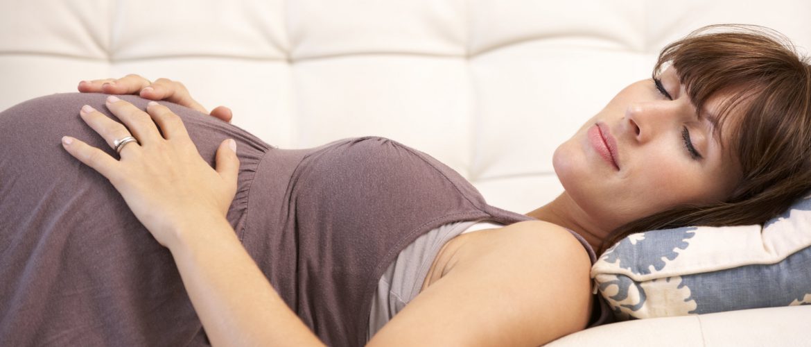 Terhes nő alszik az ágyon, közben fogja a hasát.