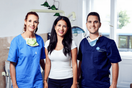 Dr. Varajti Artúr fogorvos, fogászati asszisztens és páciens állnak egymás mellett és mosolyognak a bölcsességfog eltávolítás után.