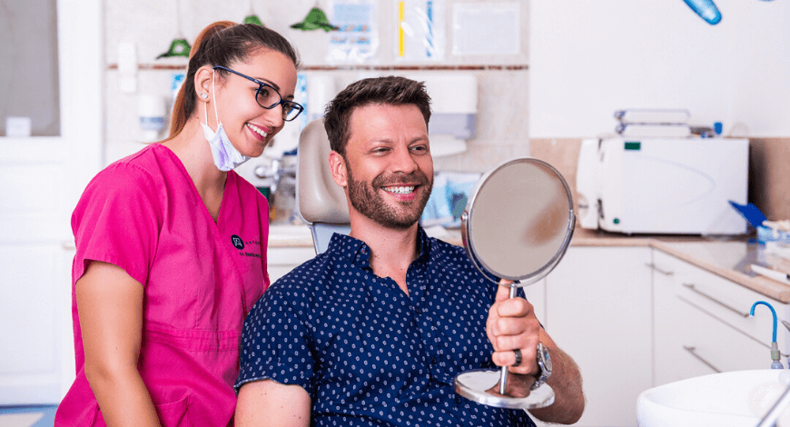 Ultahangos fogkőeltávolítás után Dr. Ökrös Petra és páciensse nézik a tükröt és mosolyognak.